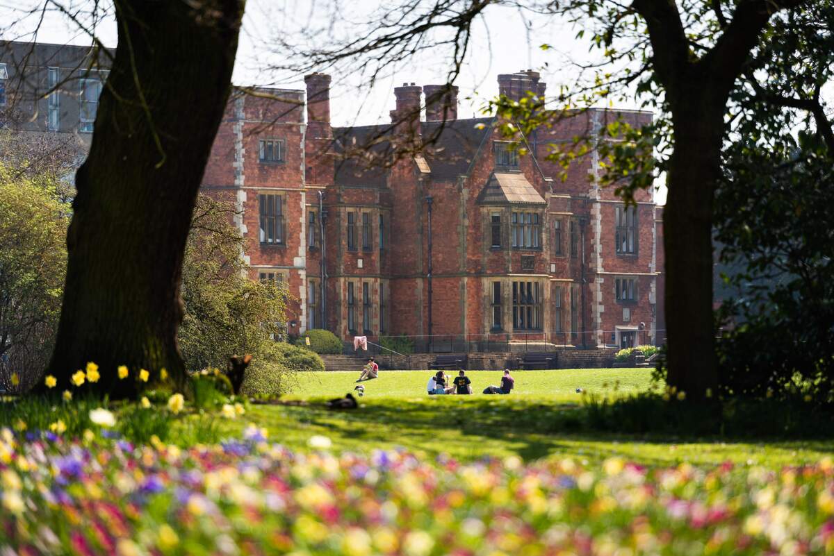 Heslington Hall with trees and people walking on the grass in front of the building